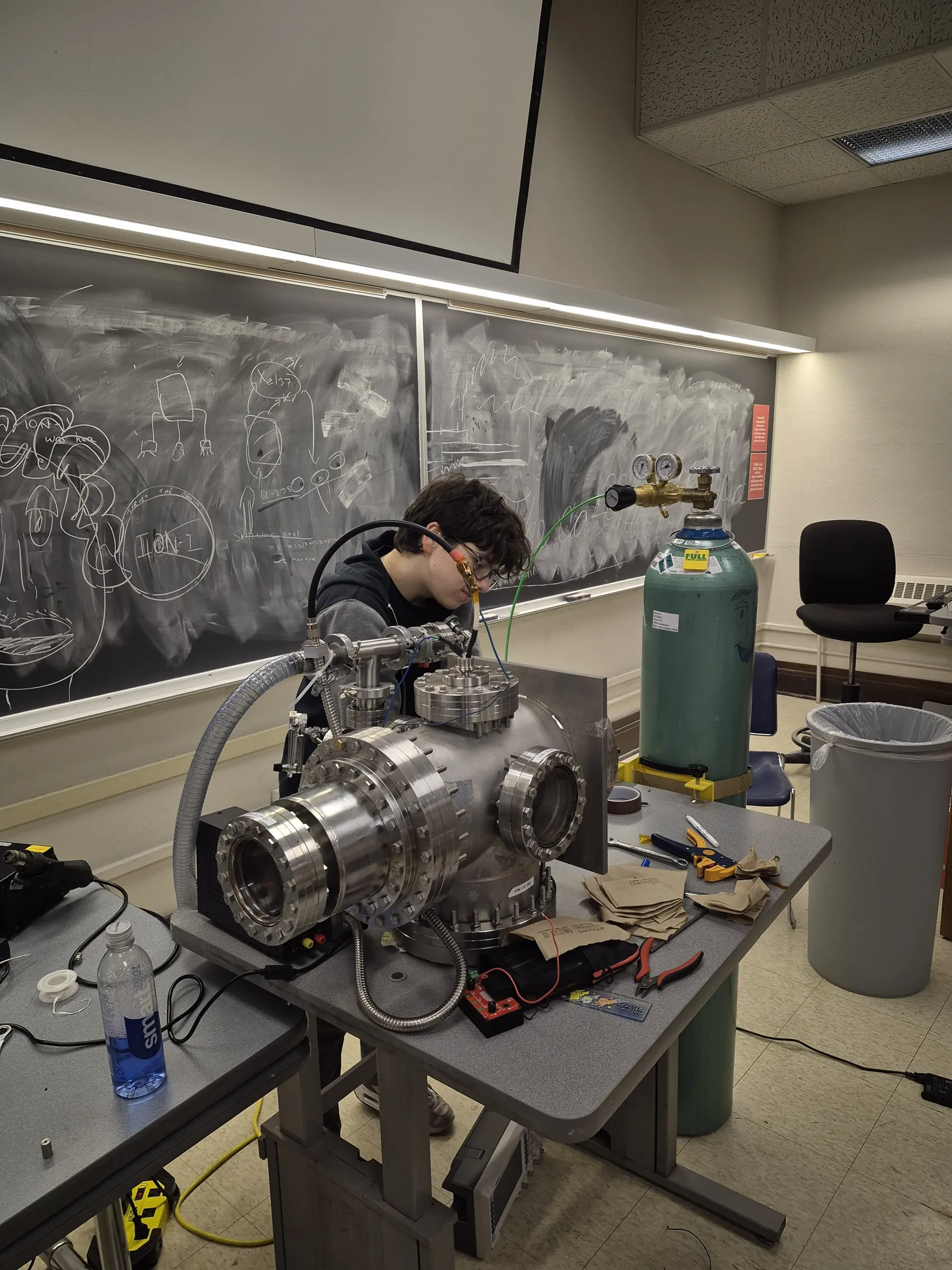 Stainless vacuum chamber on a lab bench with an argon cylinder